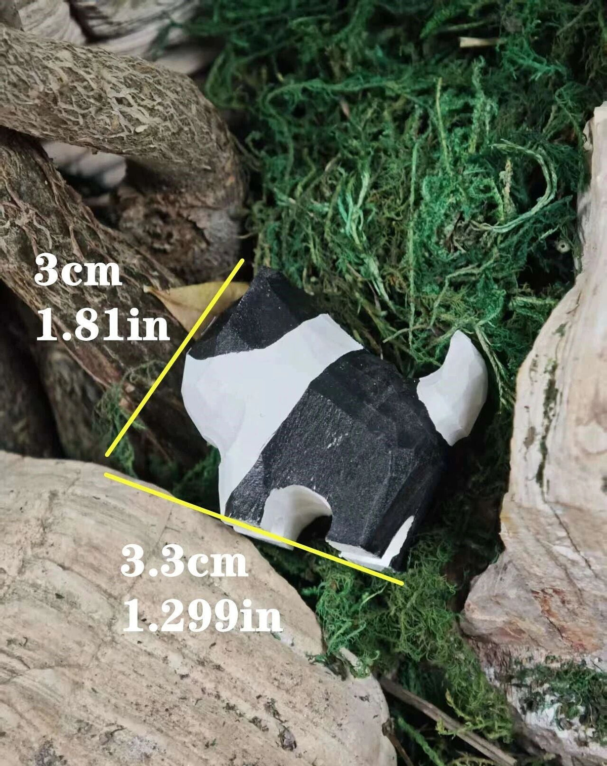 A small black-and-white striped animal toy or figurine placed among rocks and green moss, with yellow measurement lines and text showing dimensions of 3 cm by 3.3 cm.