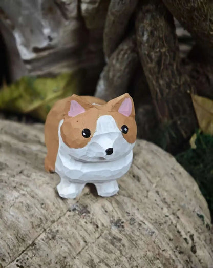 A low-poly style corgi figurine with a white and brown body, pink inner ears, and black eyes, standing on a textured stone surface with a blurred natural background.