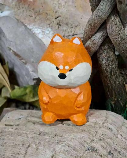 A low-poly style orange fox figurine with a white muzzle and black nose, standing on a textured stone surface with rustic wood and rocks in the background.