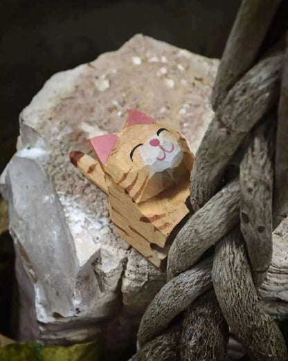 A small wooden cat figurine with a paper-like face and pink ears, resting on a rough stone beside a thick braided rope.