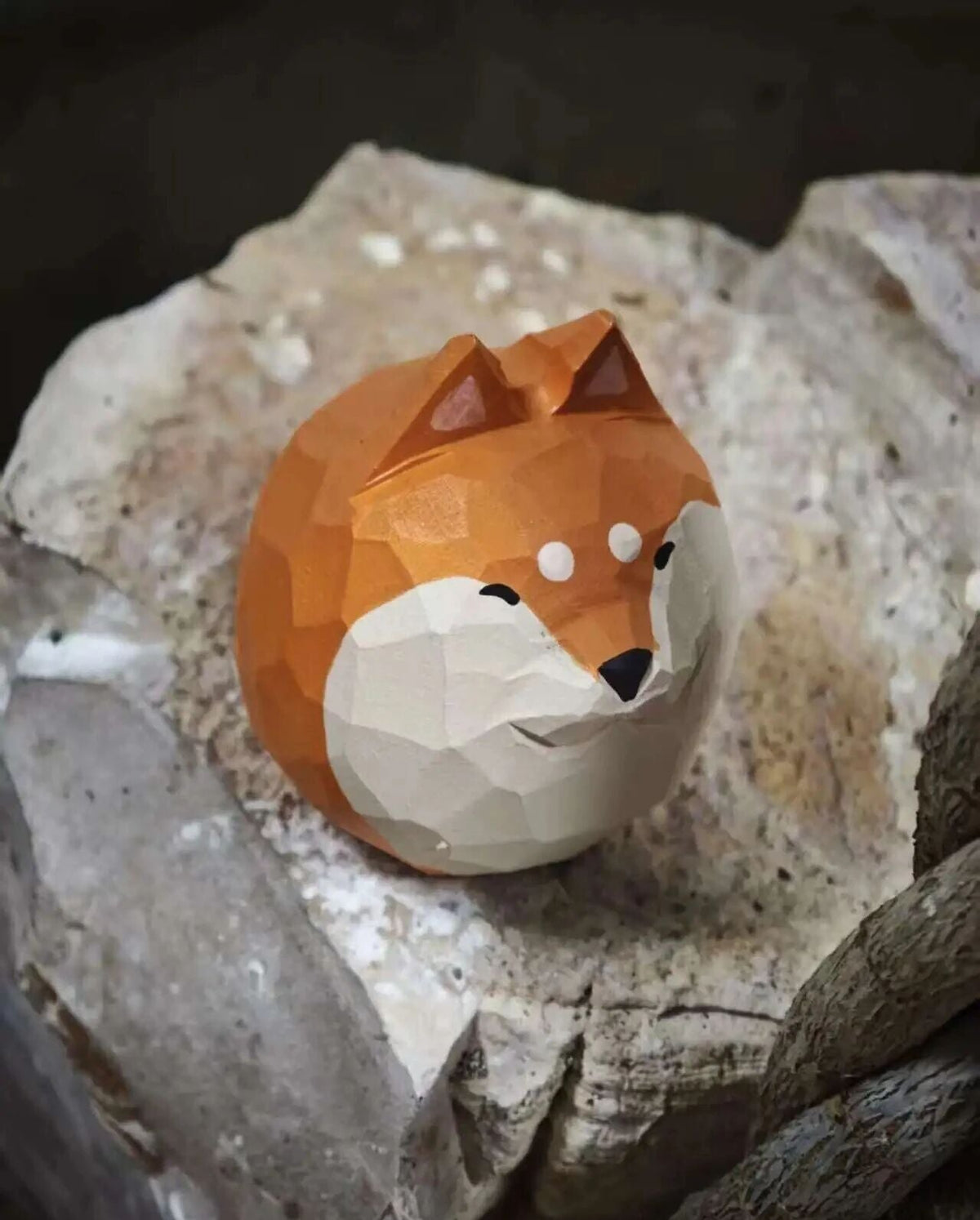 A low-poly geometric fox figurine in orange and cream, displayed on a textured gray stone surface.