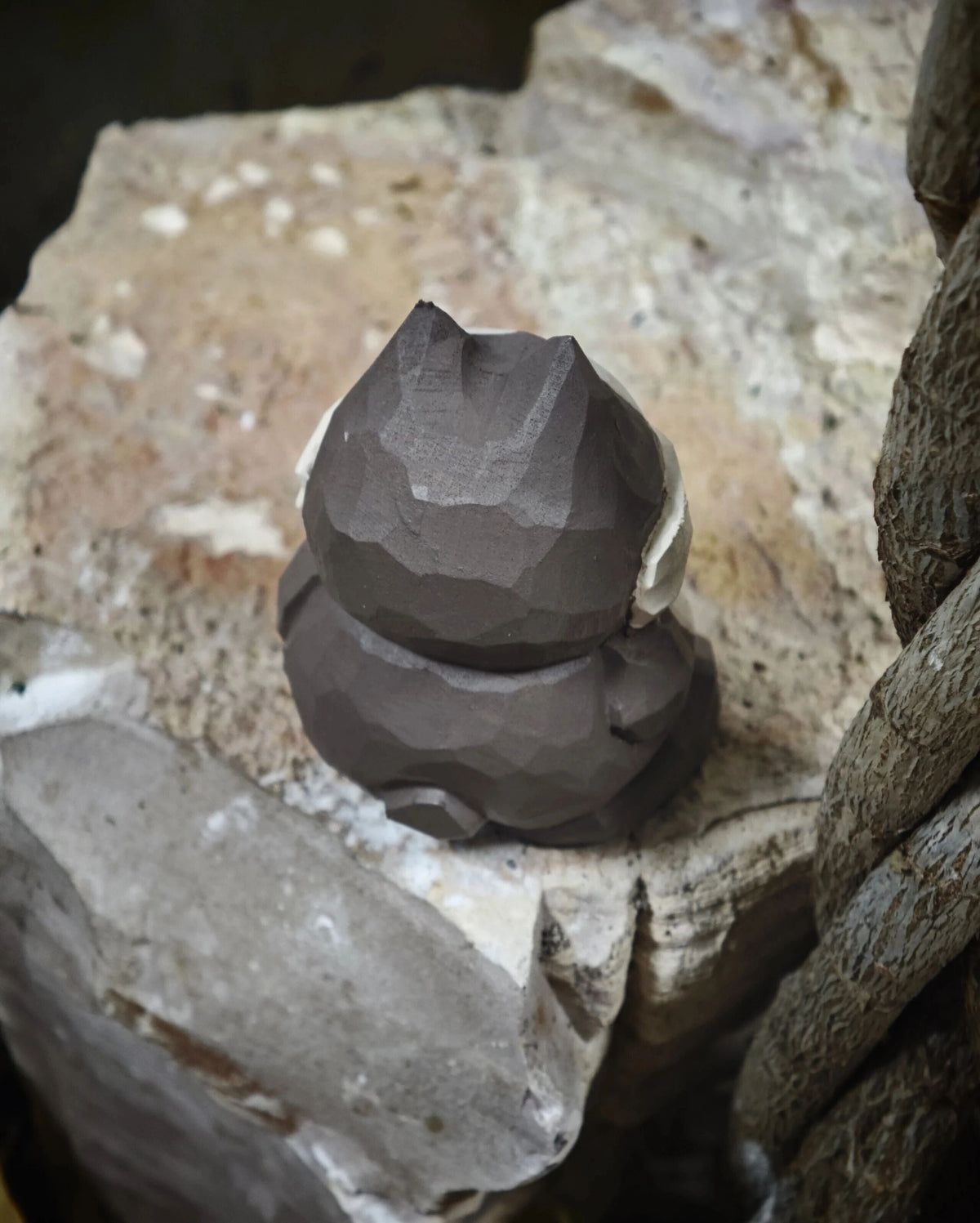 A dark gray, faceted, sculptural cat figurine sitting on rough, natural stone slabs.