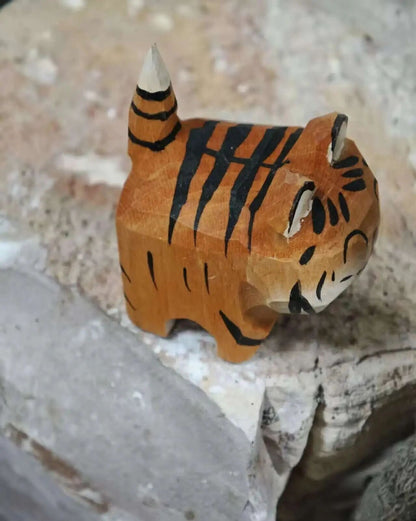A hand-carved wooden tiger figurine with black painted stripes, standing on a textured stone surface.