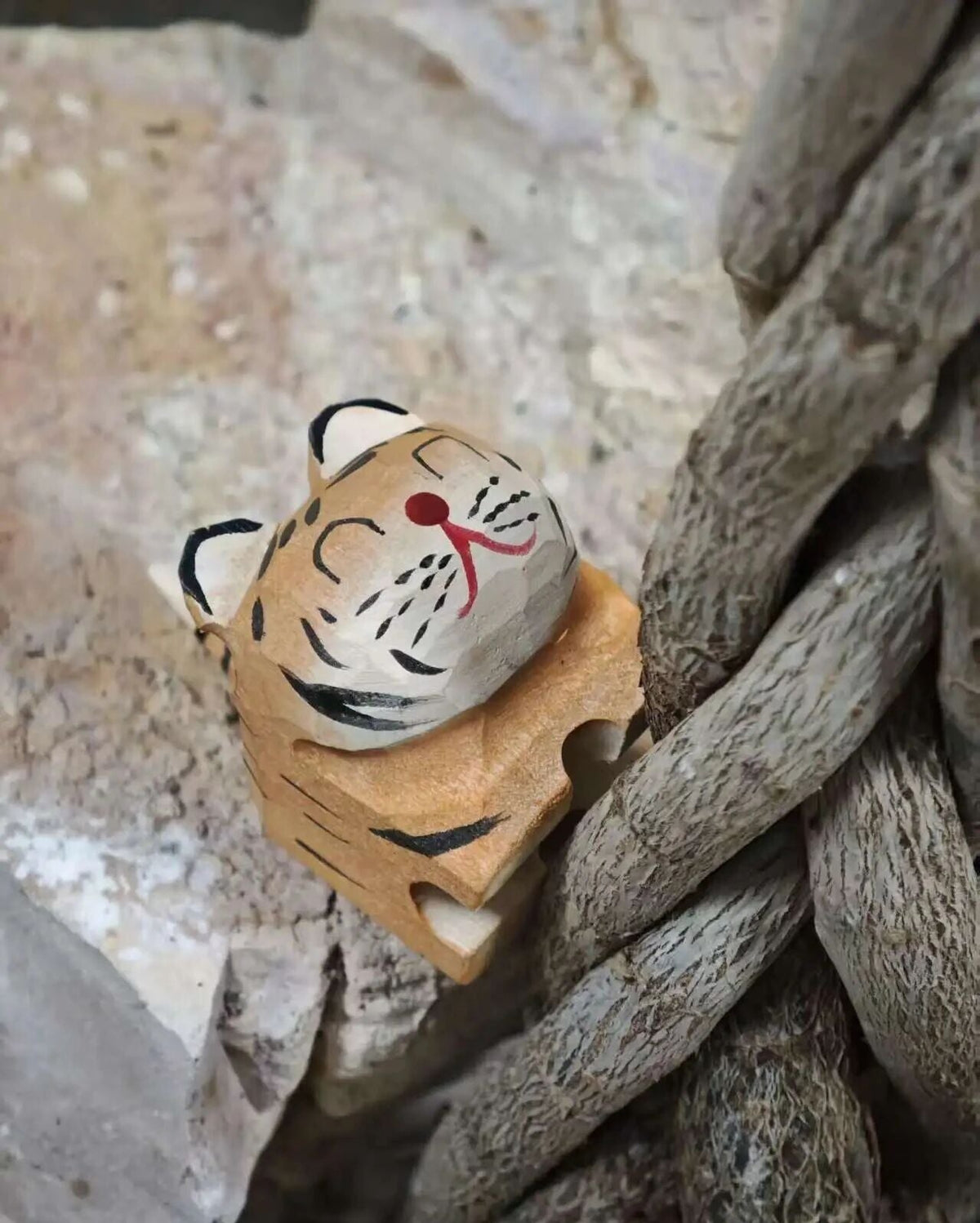 A hand-painted wooden tiger figurine with a carved base, resting on a textured stone surface next to a thick natural rope.