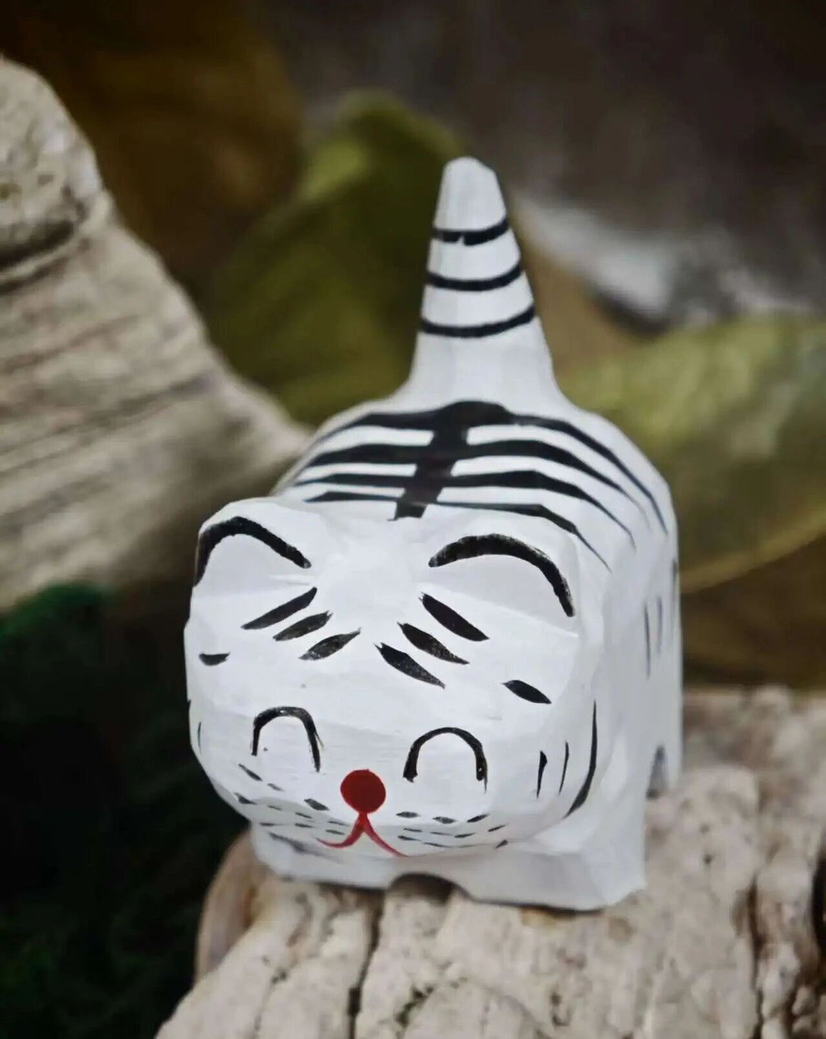 A small white carved tiger figurine with black stripes and a red nose, resting on a textured stone surface.