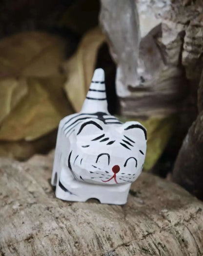 A small white tiger figurine with black stripes and a red nose, sitting on a textured stone surface with a blurred natural background.