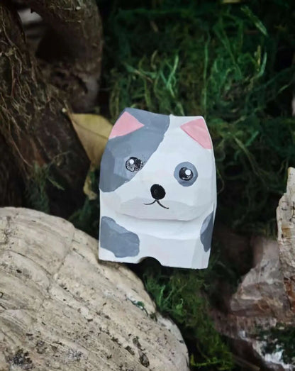 A handmade paper cat-shaped desk mat styled on a natural moss and wood surface. The cat features a white base with gray patches, pink inner ears, and simple black facial features.